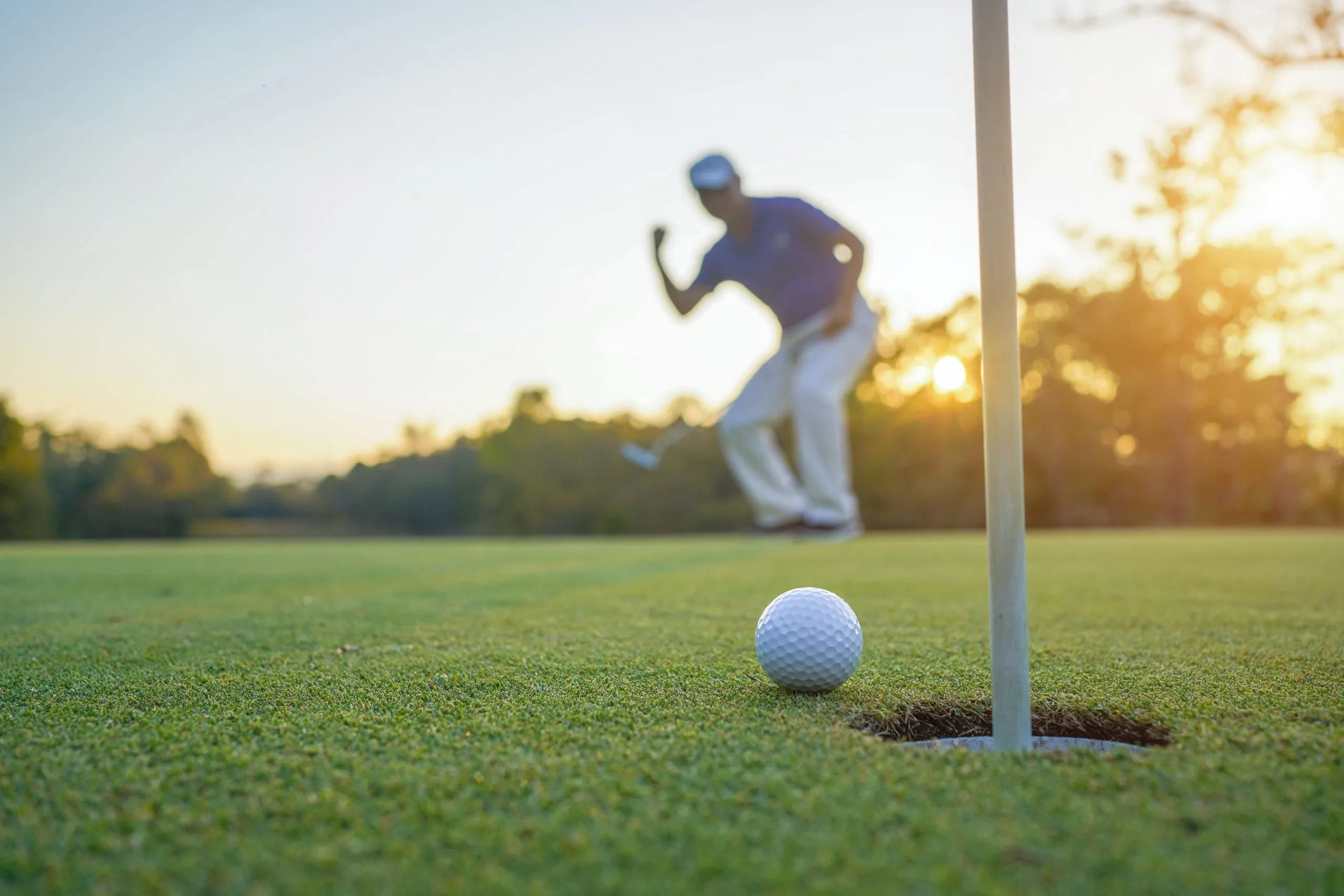 Golfer action to win after long putting golf ball on the green golf, lens flare on sun set evening time.