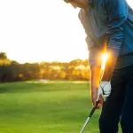 Male golf player teeing off golf ball from tee box to beautiful sunset